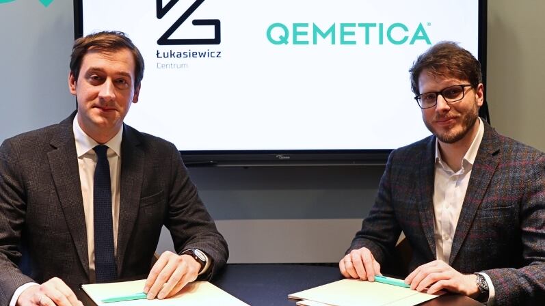 Two men in suits sat in front of a monitor