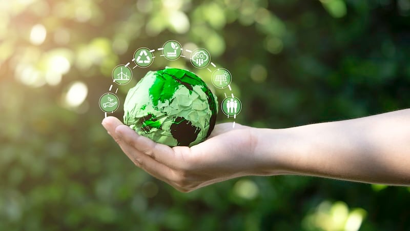a hand holding a green scrap paper globe surrounded by sustainability logos