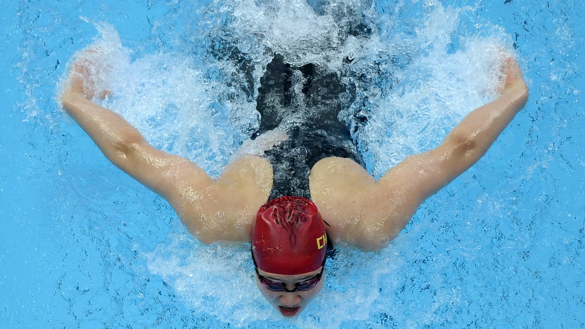 a female swimmer with a red cap and a black bodysuit doing the butterfly